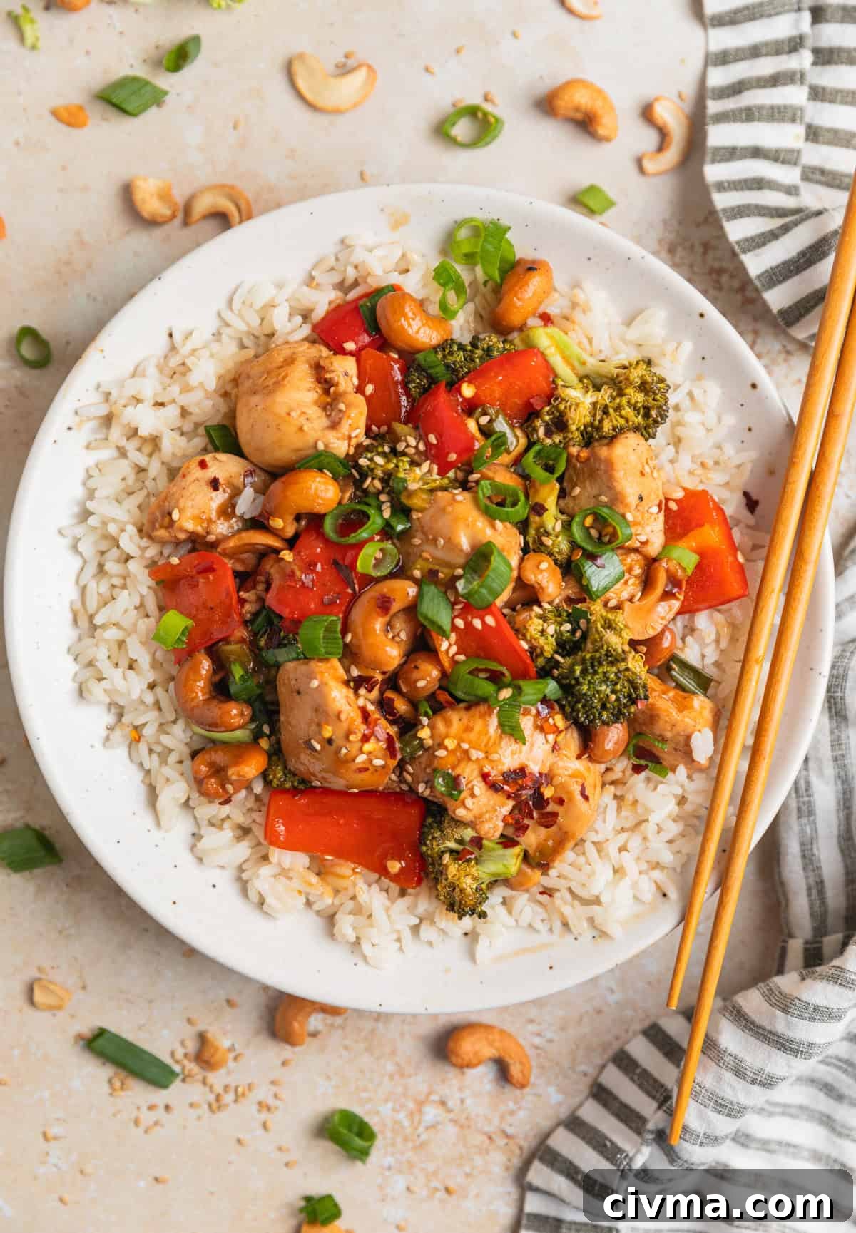 Overhead view of white dish with rice topped with cashew chicken and chopsticks propped on the plate.