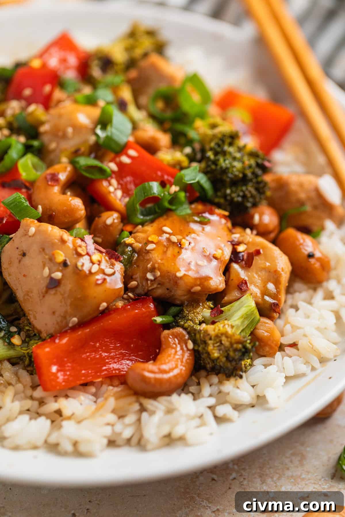 Ceramic plate with rice covered in chicken, red bell pepper, broccoli, green onion and sesame seeds.