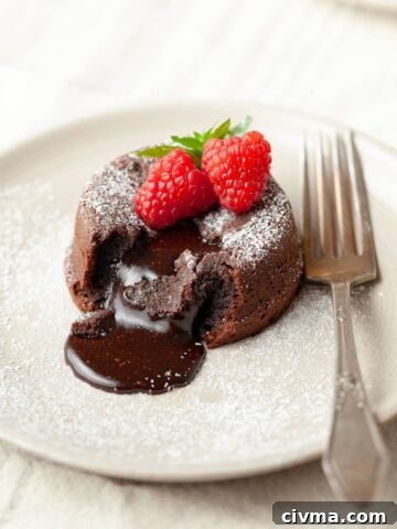 Gluten free chocolate lava cake with a molten center, topped with fresh raspberries and powdered sugar on a beige plate with a fork