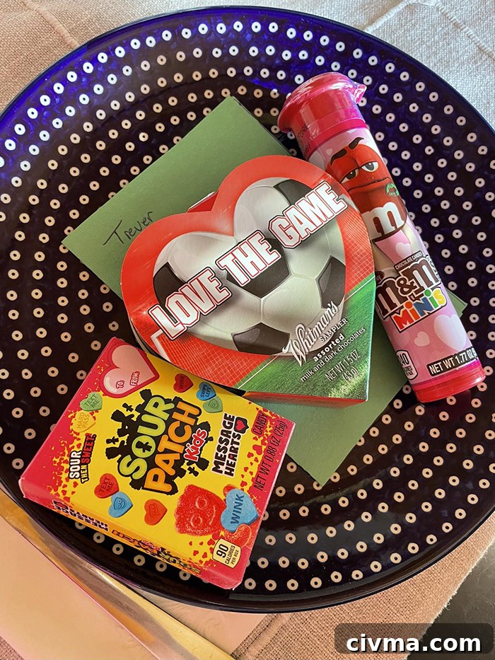 A dark blue Polish pottery plate with white polkadots with a valentine's M&M tube, a heart shaped package of candy with a note underneath it, and a box of valentines sour patch kids.
