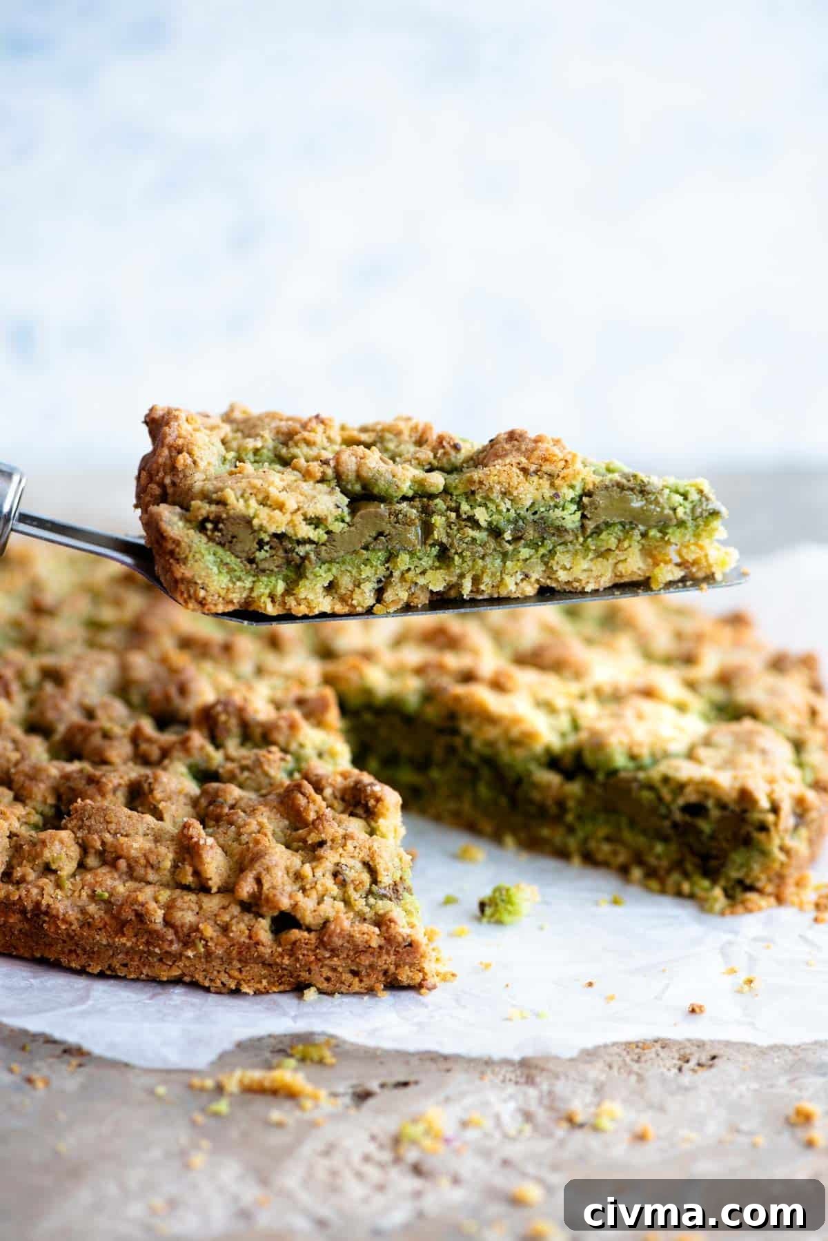 A cake slice holding up a slice of pistachio crumb cake showing a layer of pistachio in the middle.