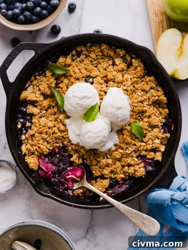 Apple blueberry crumble in a skillet, topped with three scoops of vanilla ice cream.