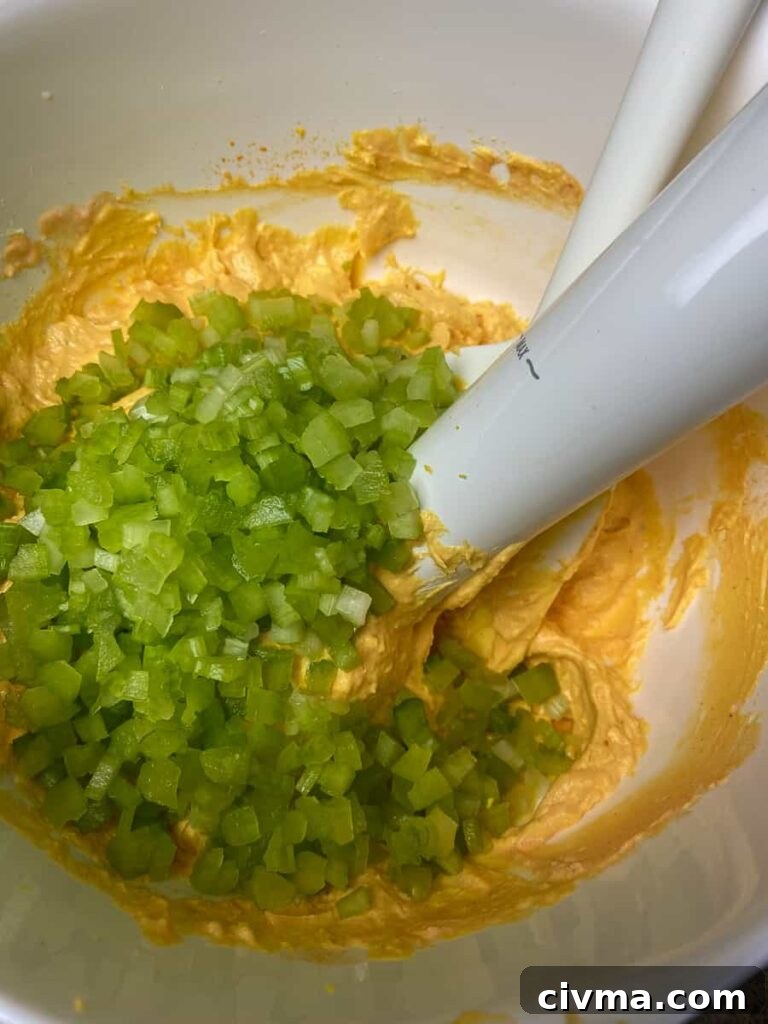 Adding chopped celery to mixing bowl with immersion blender