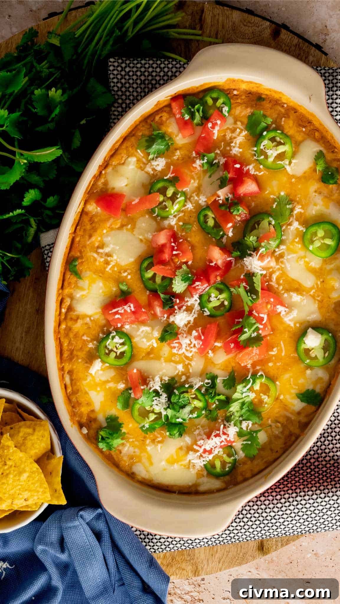 a 9 by 13 dish of Hot Mexican Bean Dip garnished with Roma tomatoes, cilantro, and sliced jalapenos.