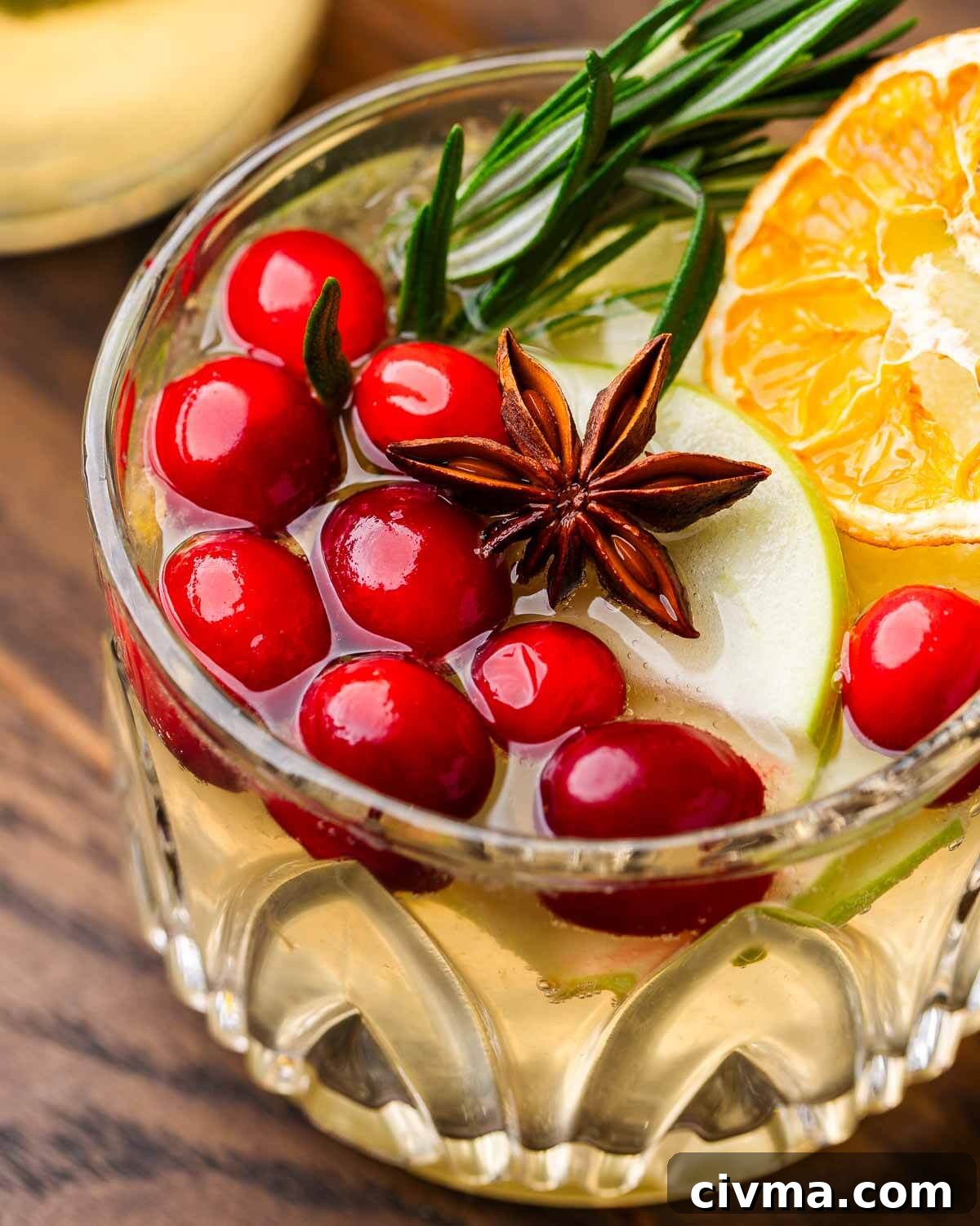Sangria with cranberries, star anise, and rosemary in small glass.