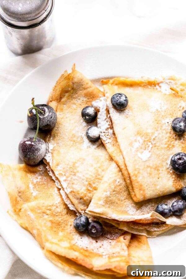 Authentic French Crepes Recipe 9 Four thin pancakes on a white plate topped with berries.
