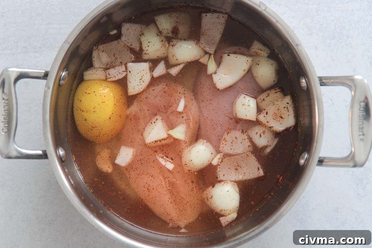 chicken in a pot with water, onions, and lemon.