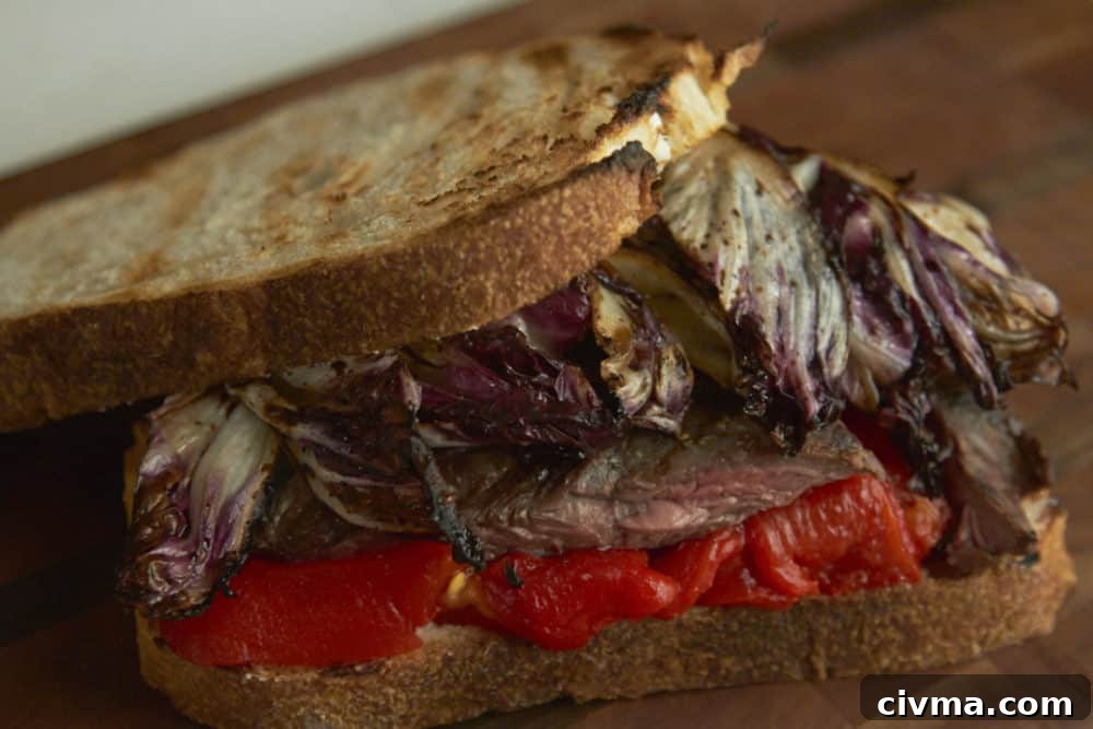 A steak sandwich with radicchio and red peppers on a wooden cutting board.