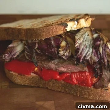 A steak sandwich with radicchio and red peppers on a wooden cutting board.
