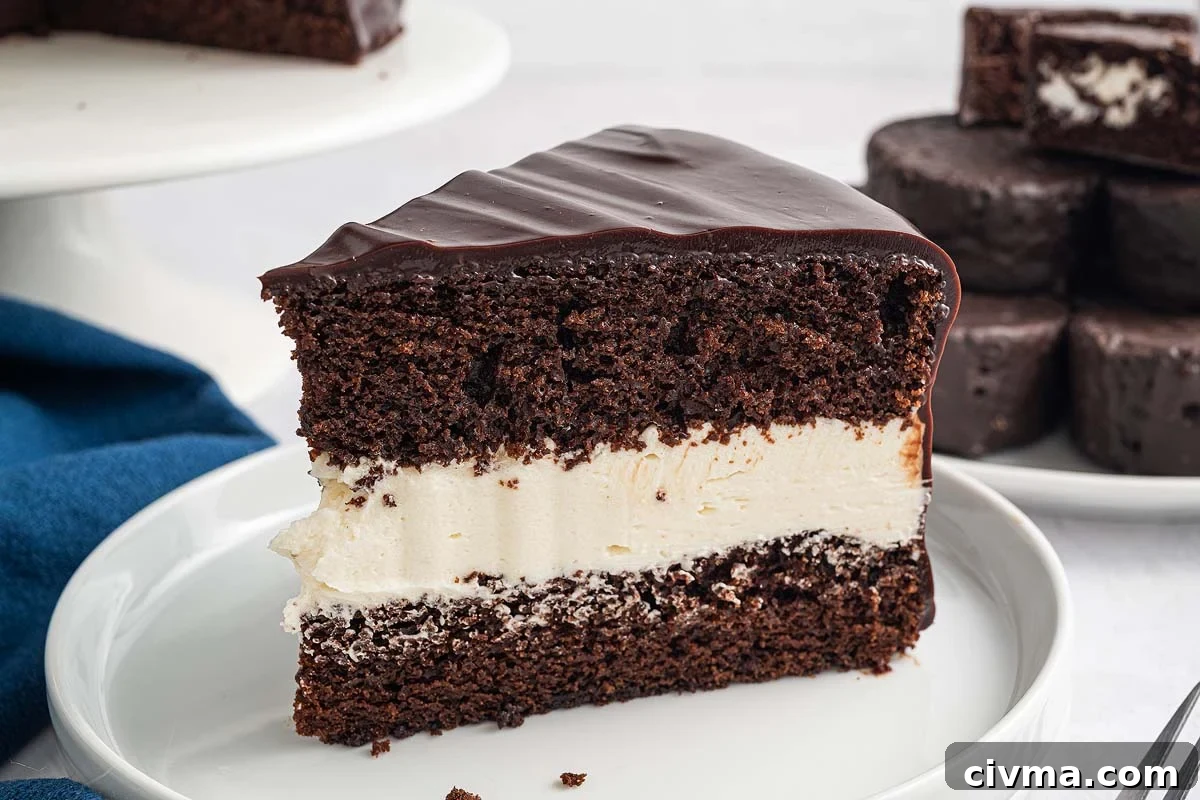 A slice of Ding Dong Cake with a thick cream filling and glossy chocolate icing sits on a white plate.