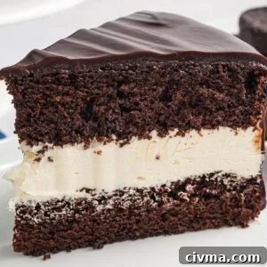 A slice of Ding Dong Cake with creamy white filling and glossy chocolate icing on a white plate.
