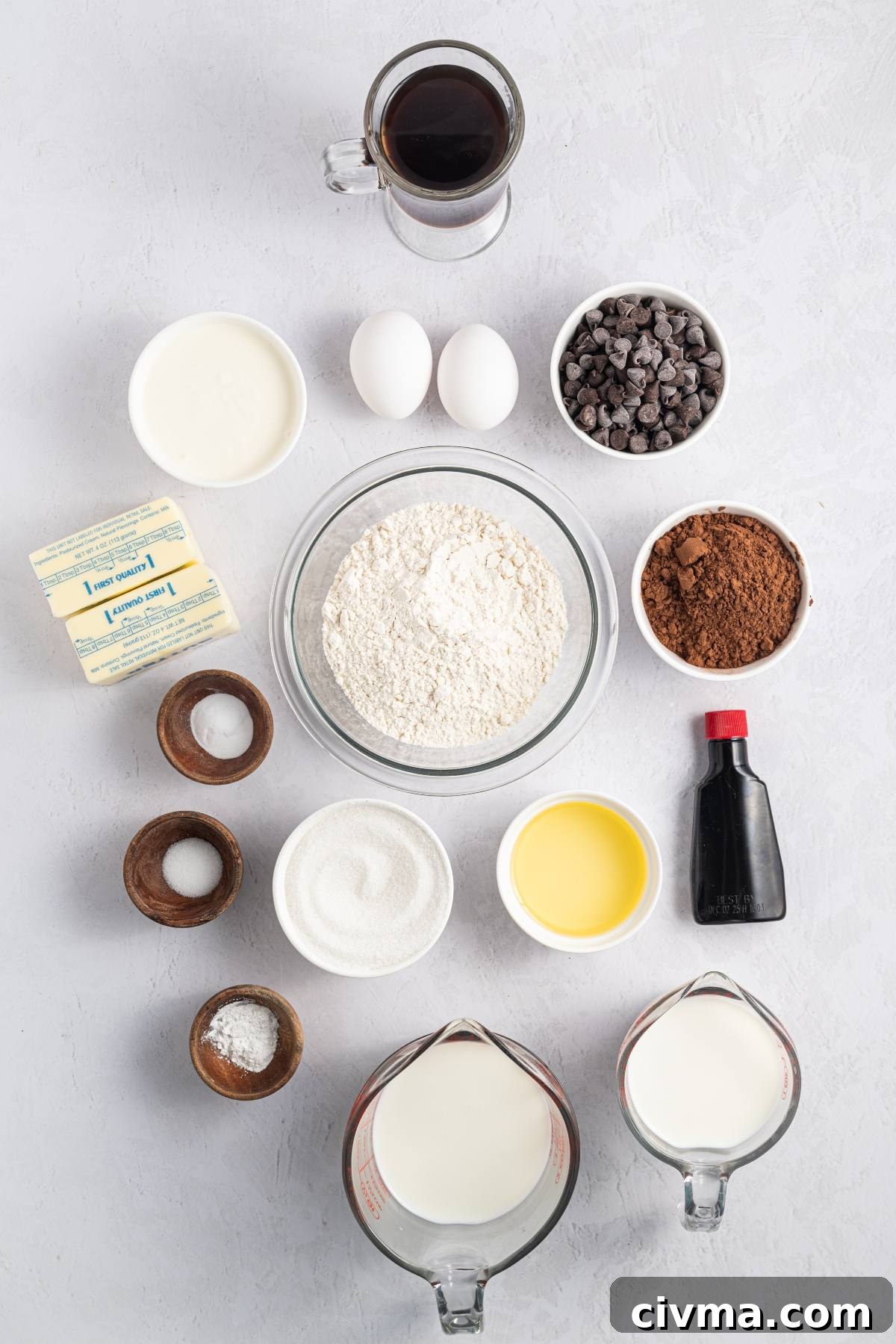 Baking ingredients arranged on a light surface, including flour, eggs, sugar, chocolate chips, cocoa, and milk.
