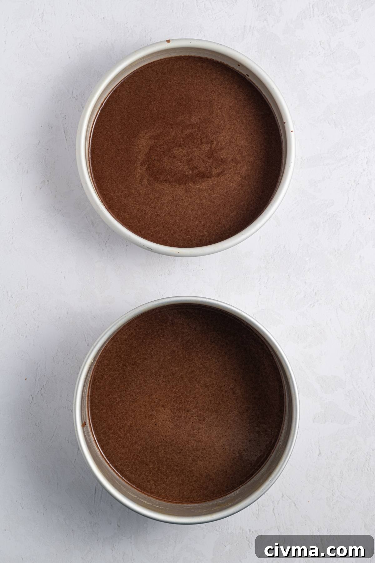 Two round cake pans filled with chocolate cake batter, placed on a light-colored surface.