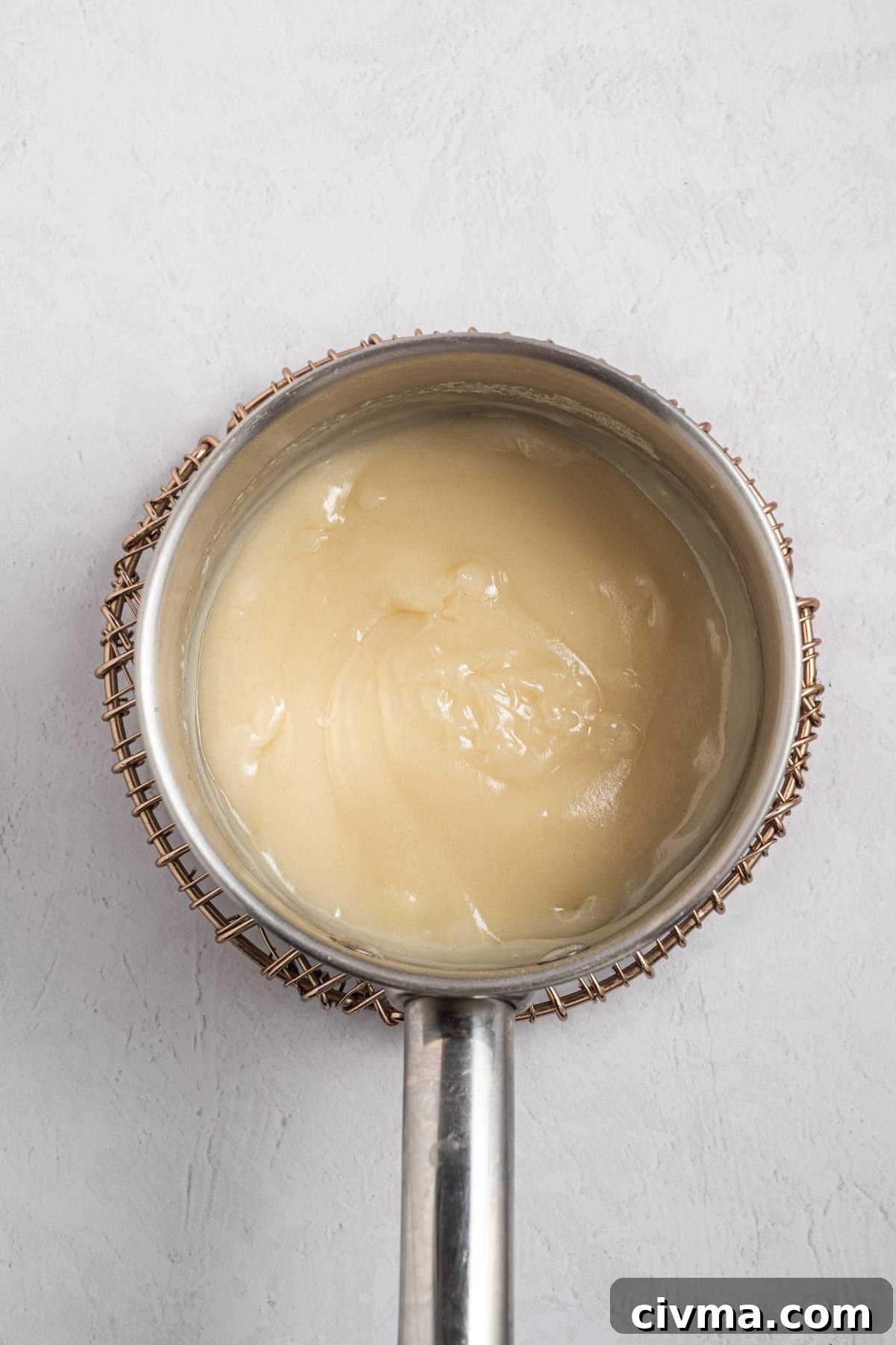 A saucepan filled with a thick, creamy white mixture on a light textured surface.