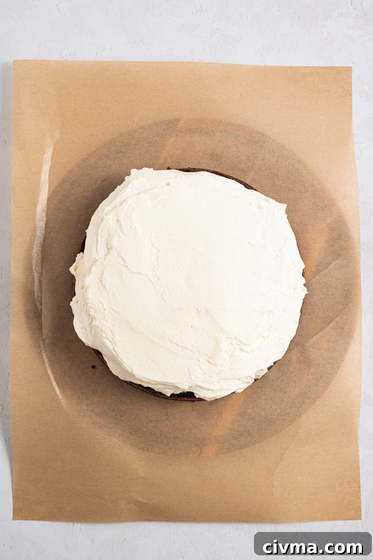 A round cake with white frosting on parchment paper, viewed from above.