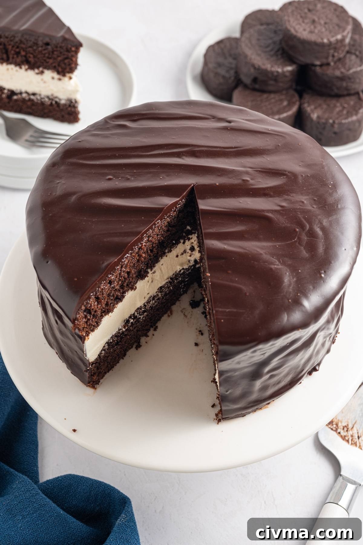 Chocolate cake with a creamy white filling, covered in glossy chocolate glaze, with one slice cut out.