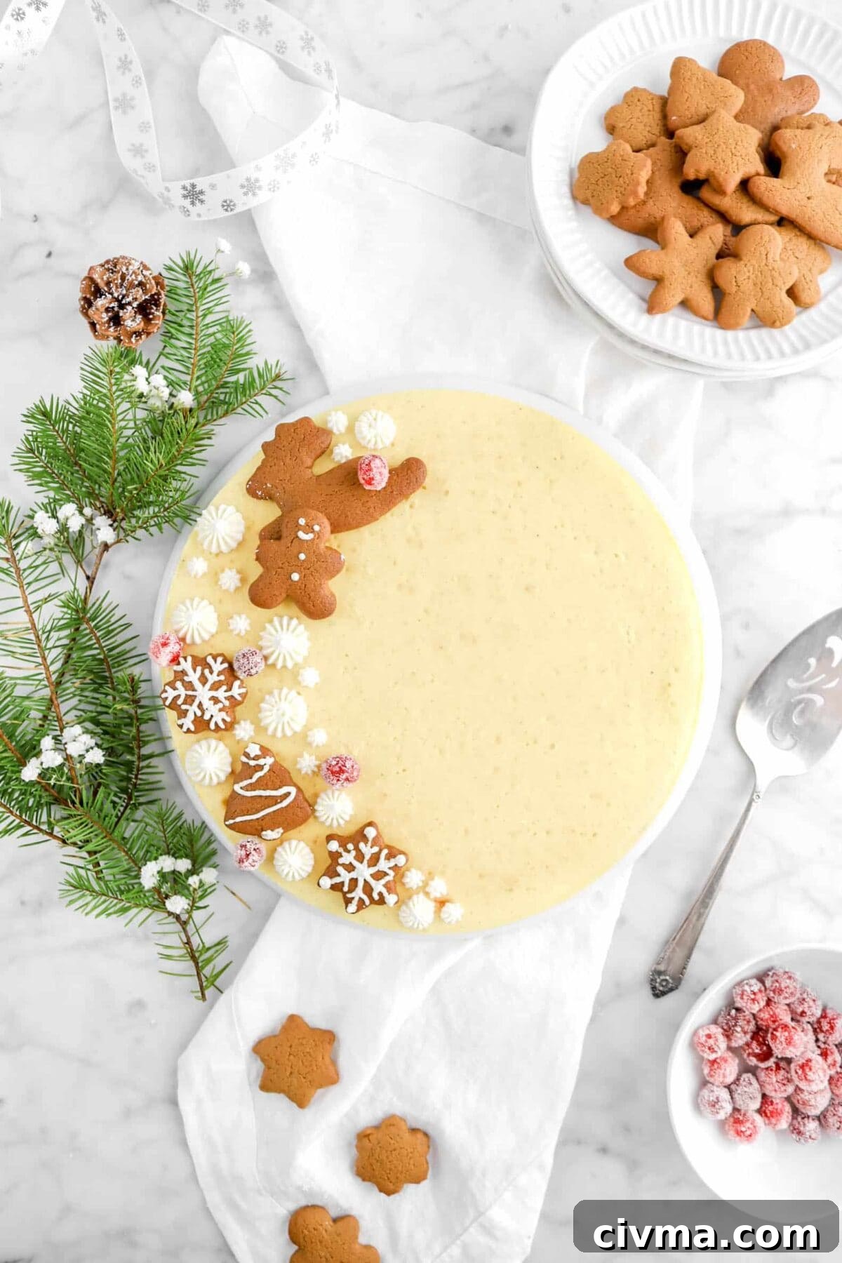 overhead shot of eggnog cheesecake with gingerbread cookies, flowers, pine, bowl of sugared cranberries, and white napkin