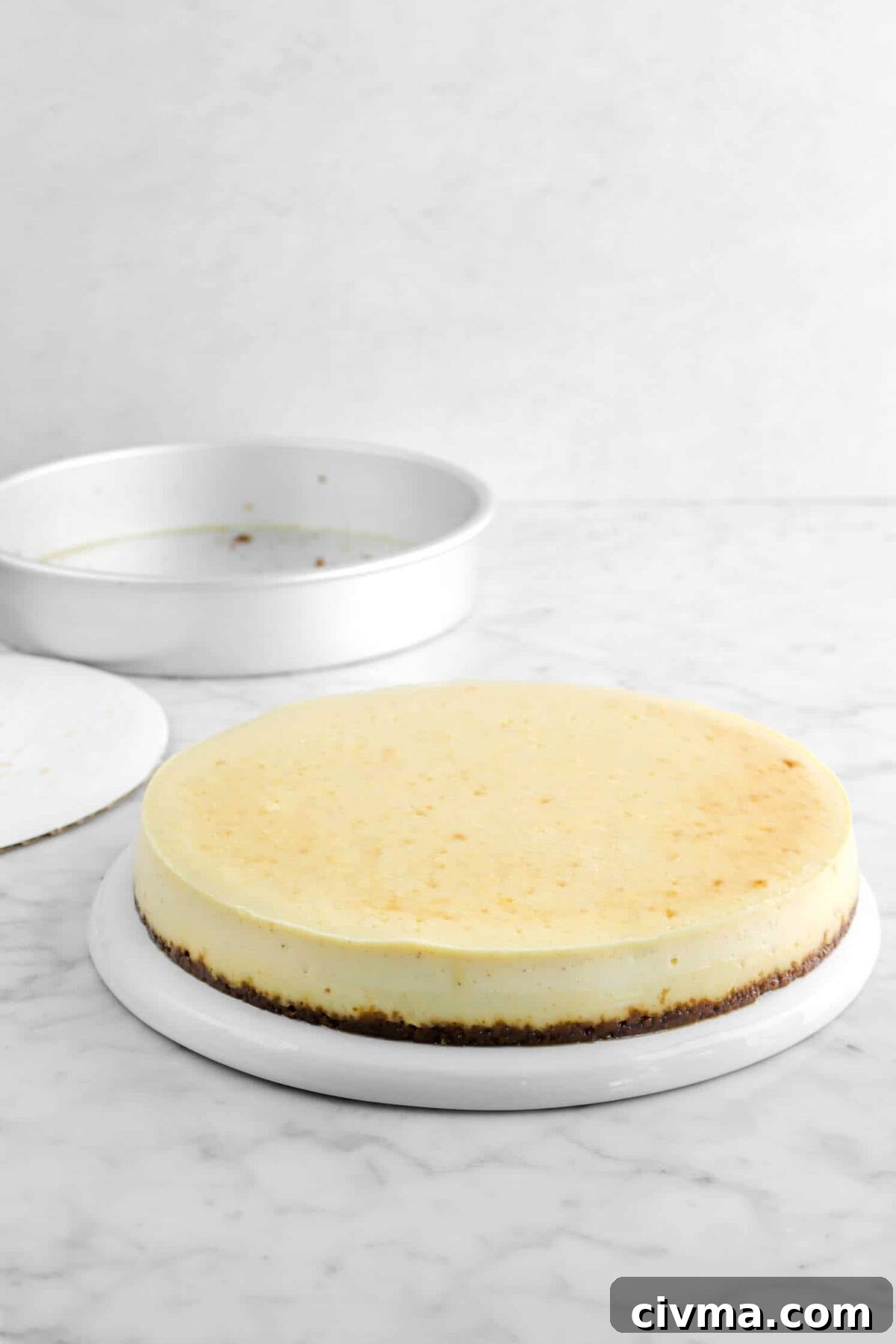 cheesecake on upside down plate with cake board and cake pan behind