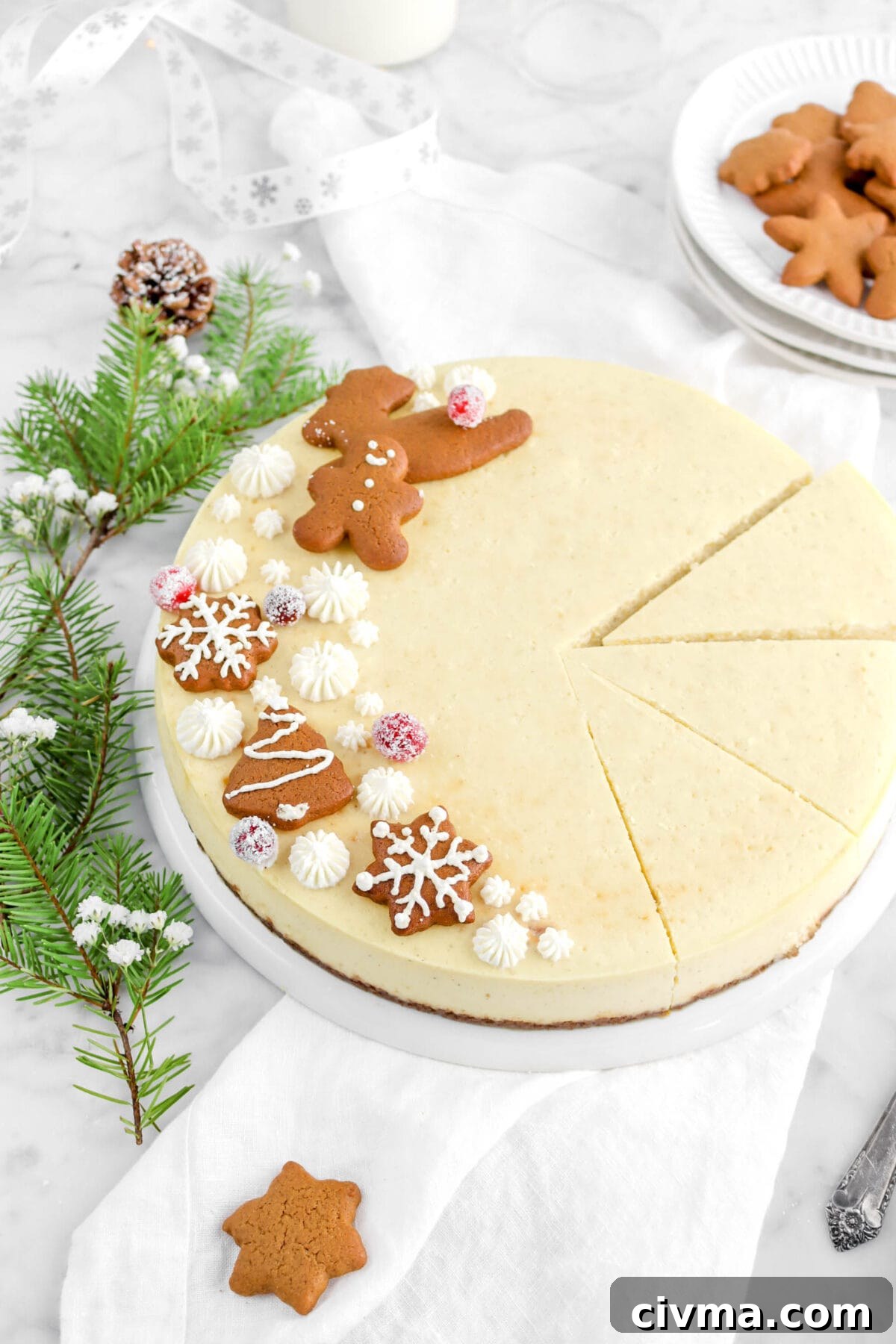eggnog cheesecake with three slices cut on upside down white plate with gingerbread cookies, sugared cranberries, and pine branches