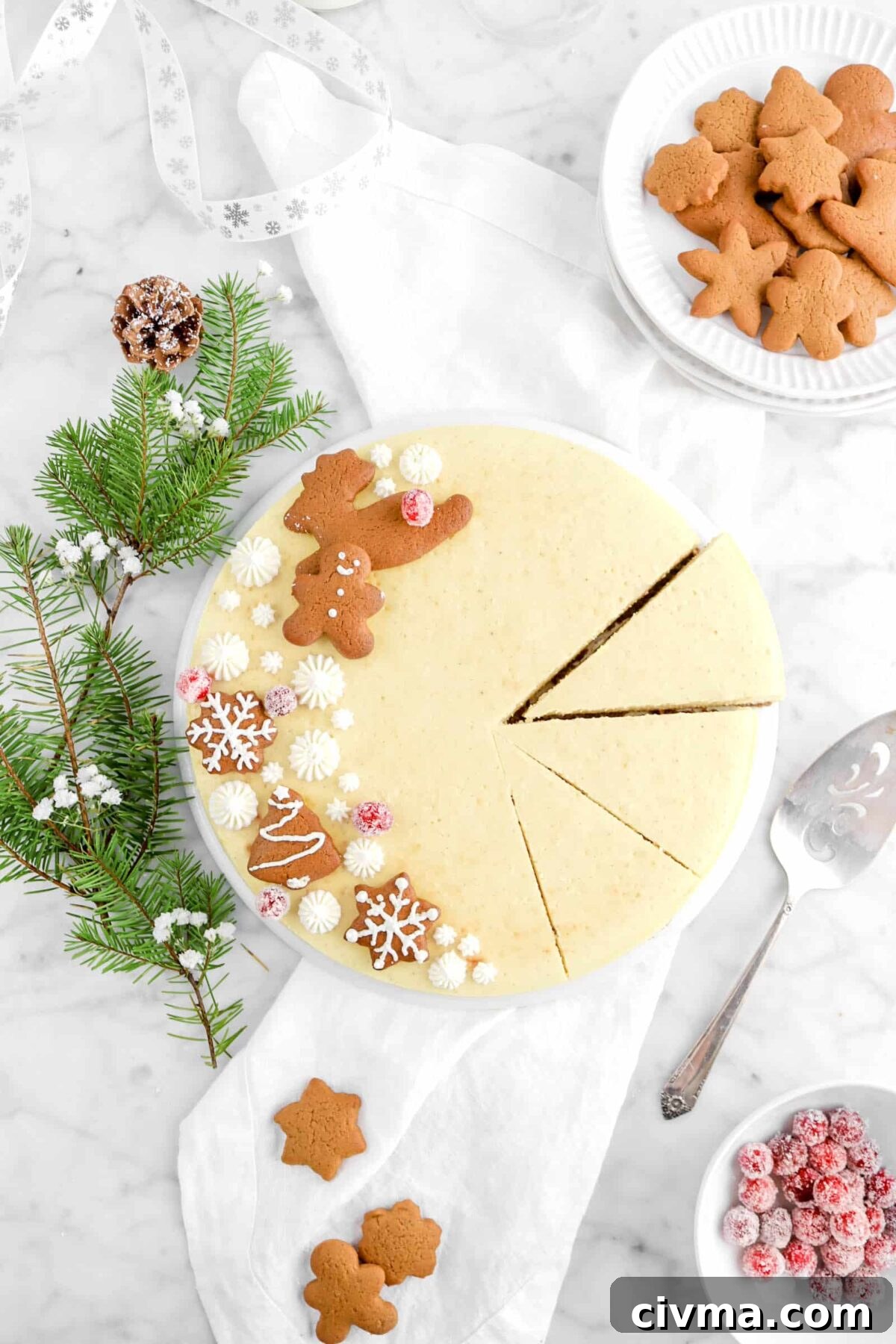 overhead of eggnog cheesecake on white plate on top of white napkin with cake server, bowl of sugared cranberries, and plate of cookies