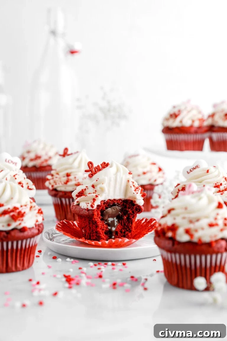 A red velvet cupcake with cream cheese frosting sits on a white plate, its wrapper peeled back to reveal a molten chocolate center.