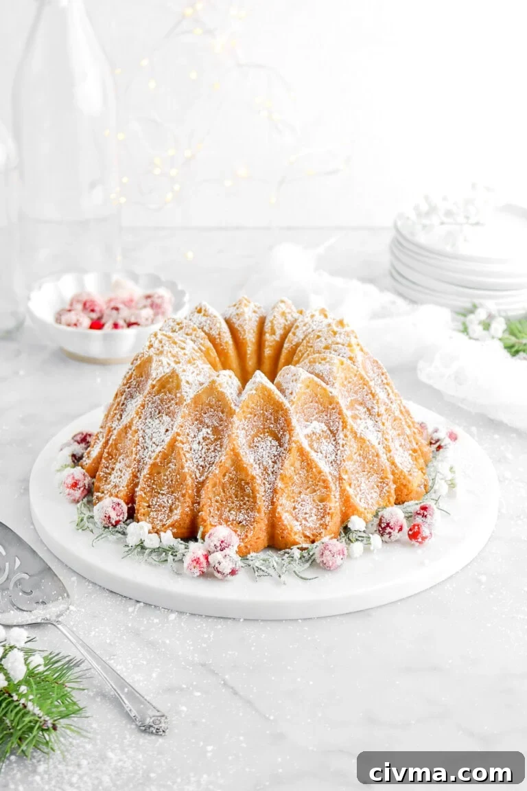 eggnog pound cake with rosemary and cranberries on marble cake plate with bowl of cranberries behind and white cheesecloth.