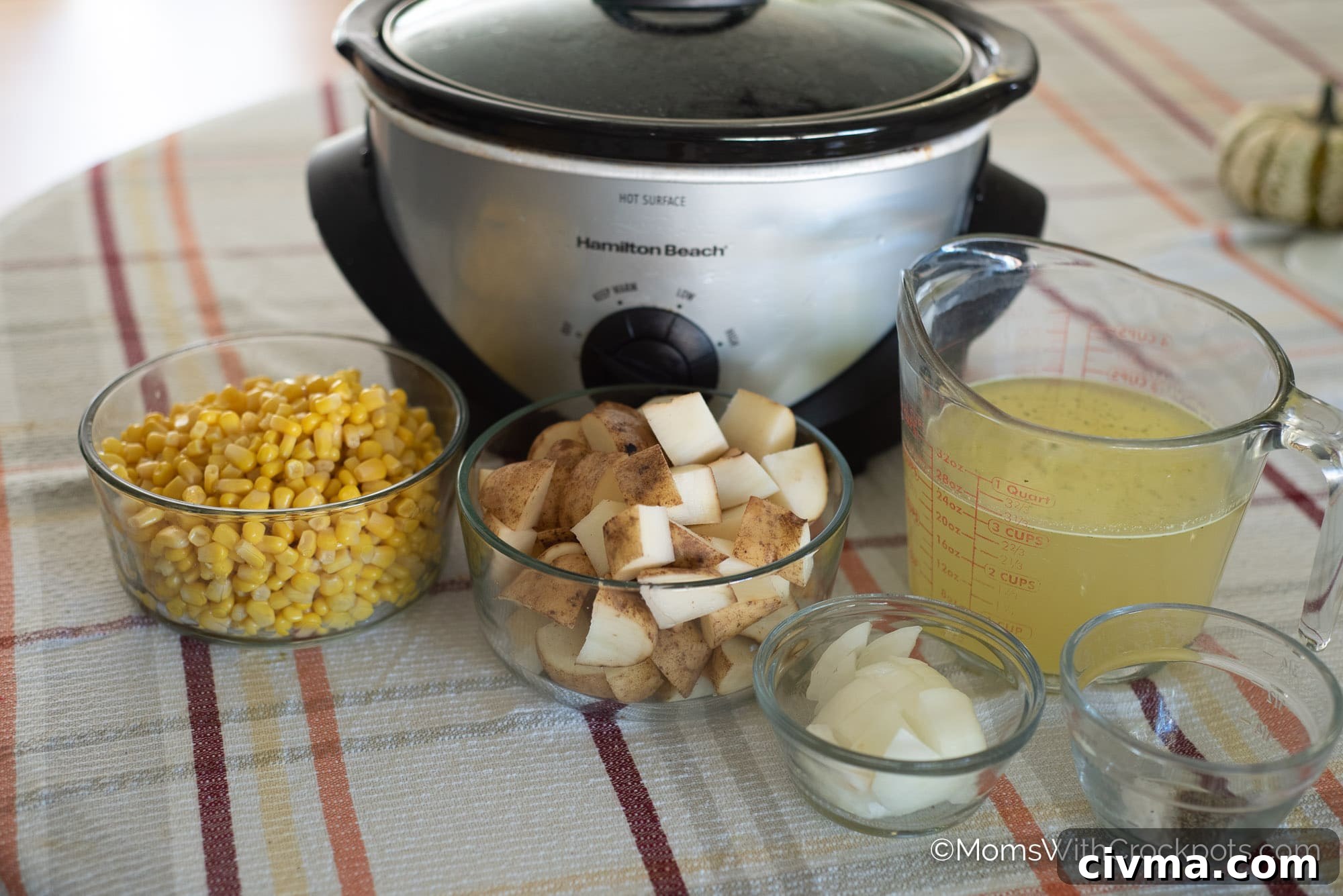 Crockpot, potatoes, corn, broth, and onion in bowls on table