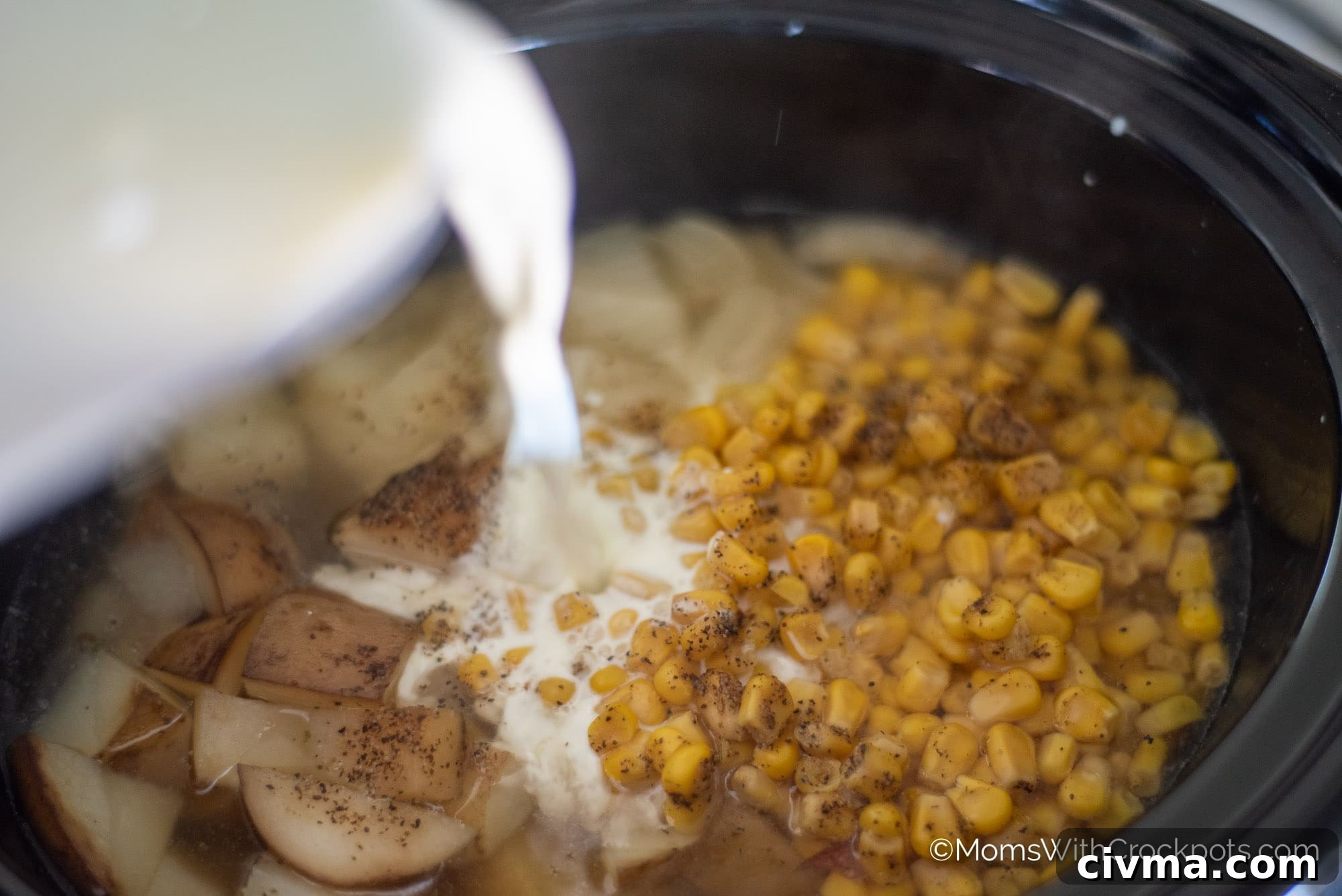 Half and half being poured into crock pot with corn and potatoes
