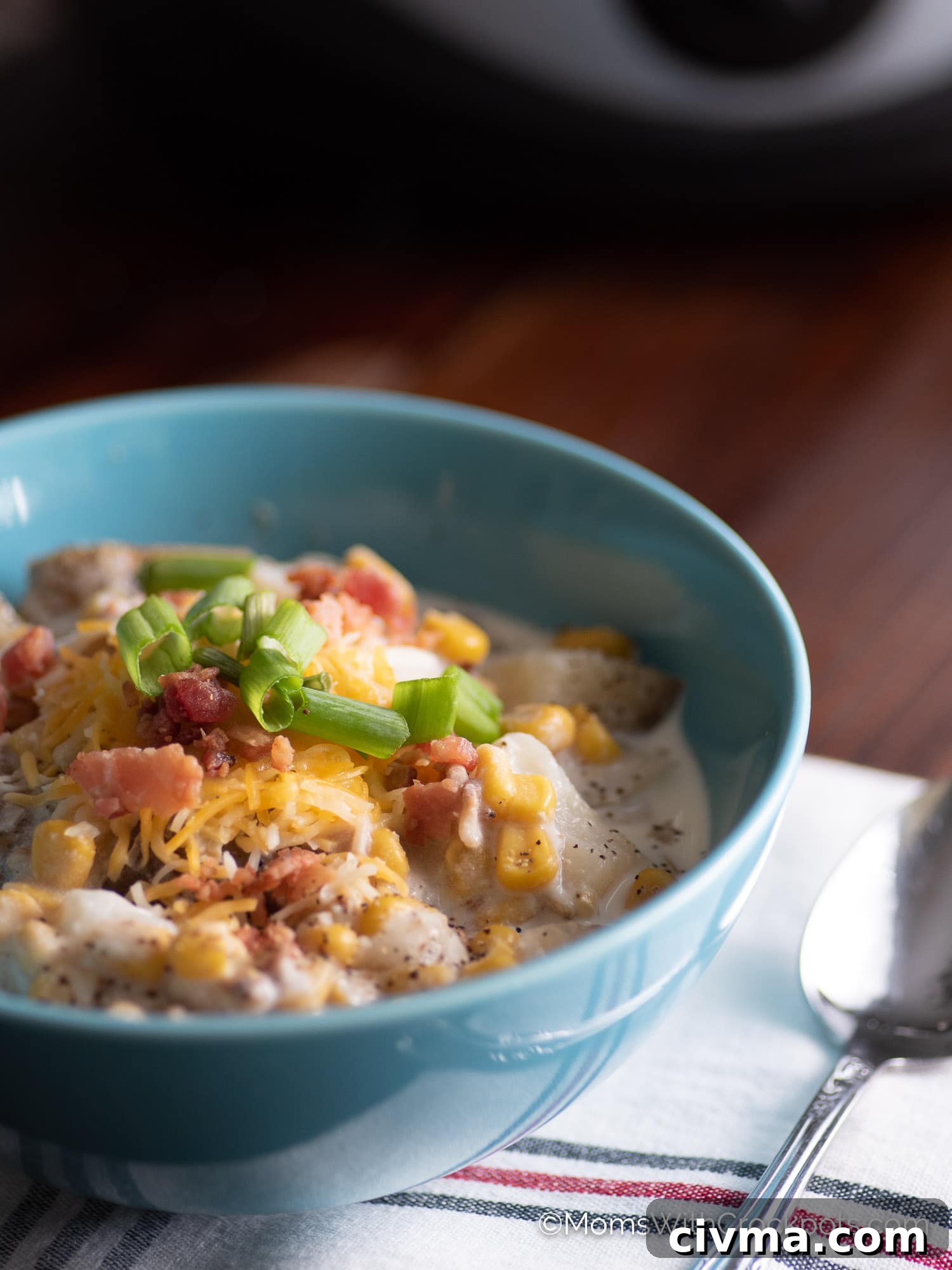 Slow Cooker Bacon Corn Chowder in blue bowl with cheese, bacon, and green onion