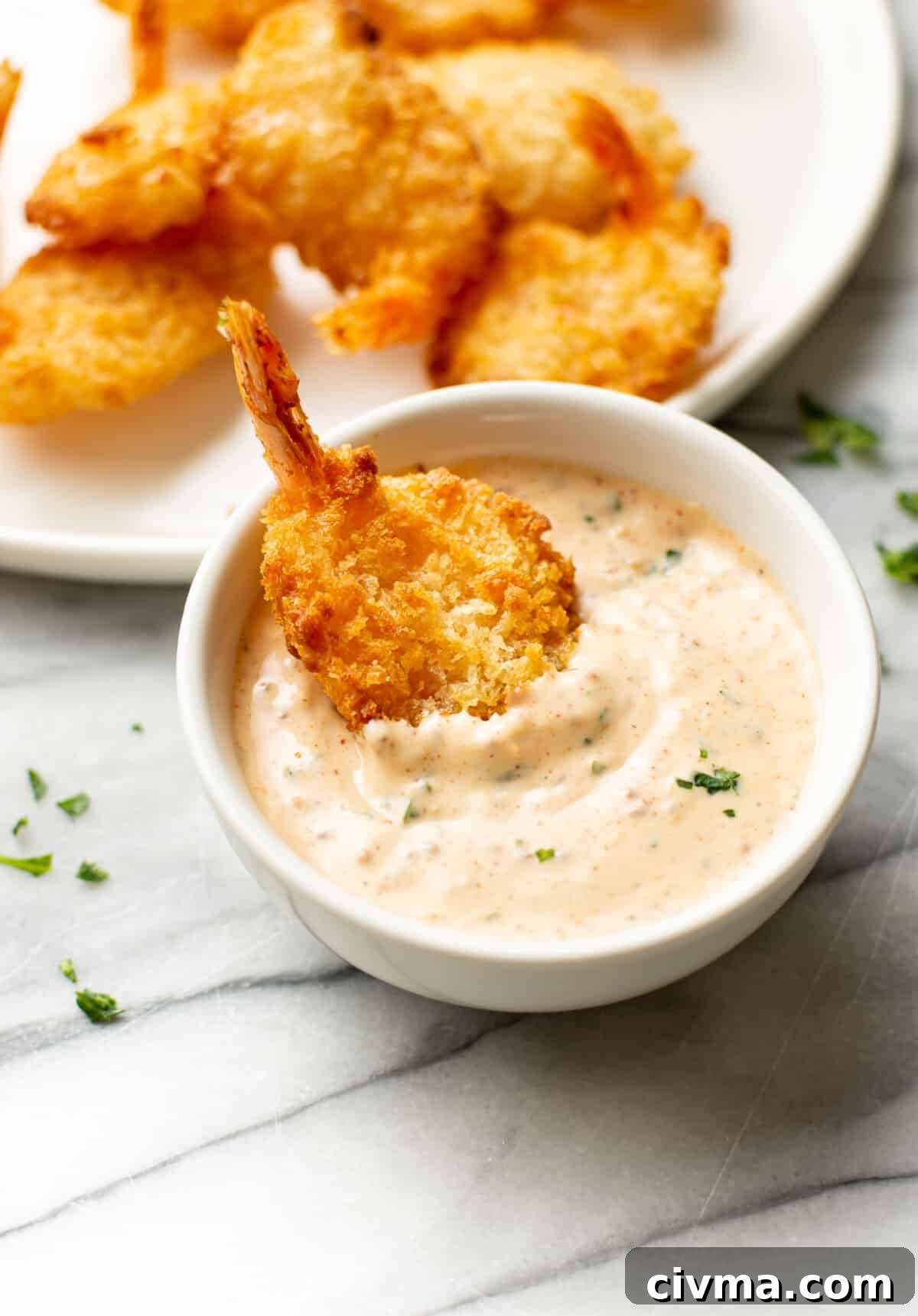 dipping breaded shrimp into a bowl of remoulade sauce