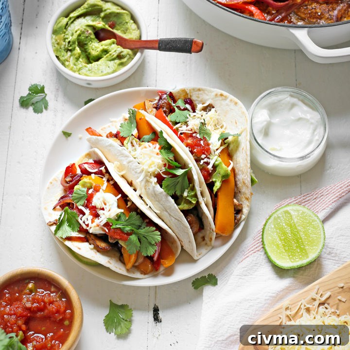 a plate of vegetarian fajitas on a white wooden table with bowls of guacamole, salsa, and sour cream