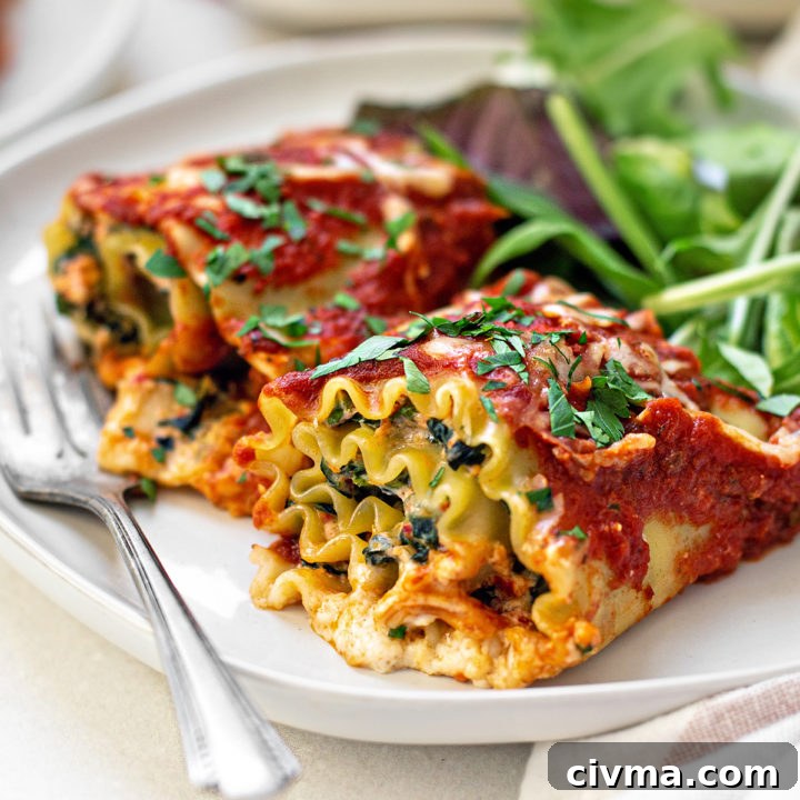 two spinach lasagna rolls on a white plate with a fork and green salad