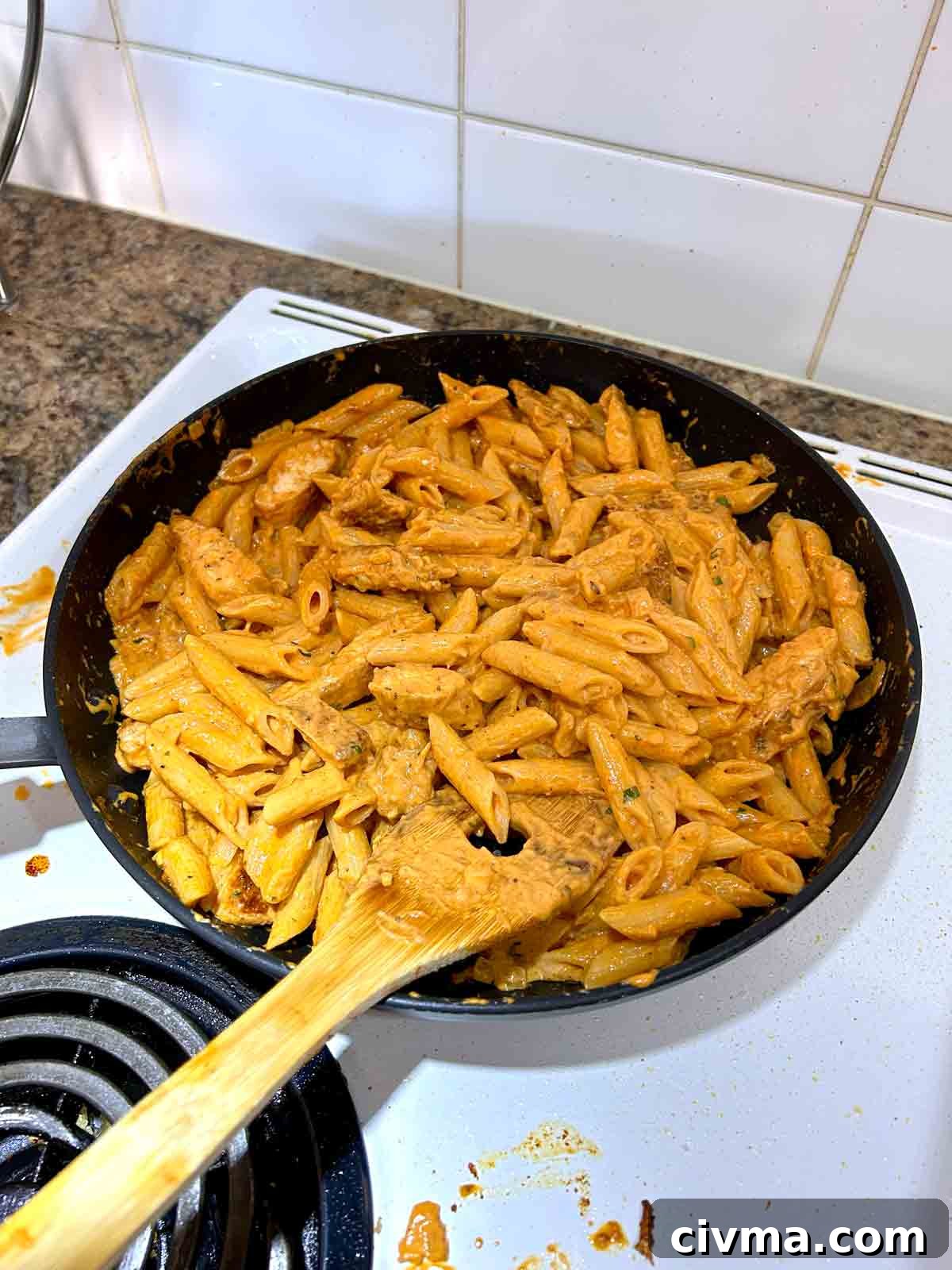 chicken and pasta being tossed with sauce in pan.