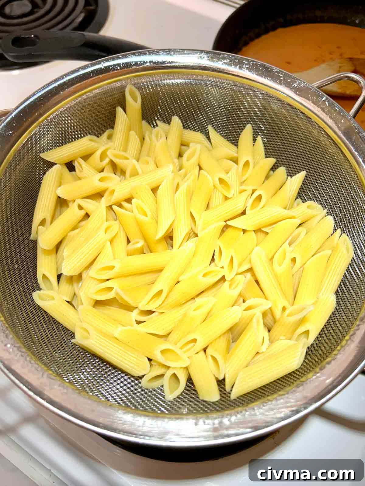 cooked penne being drained in colander.