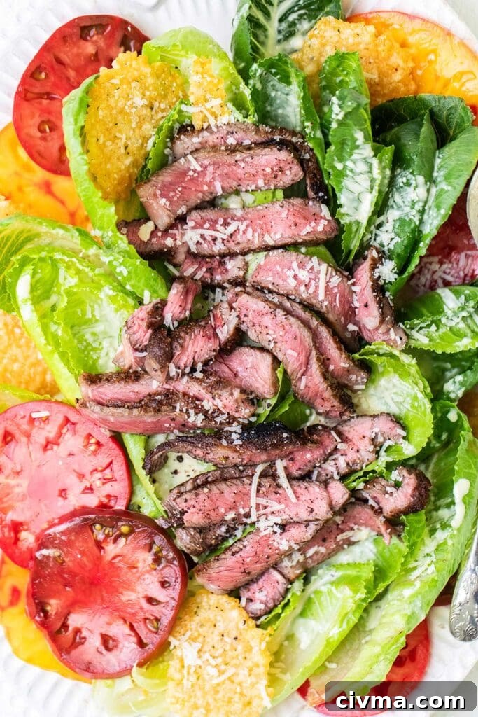 A steak caesar salad with large slices of heirloom tomatoes.