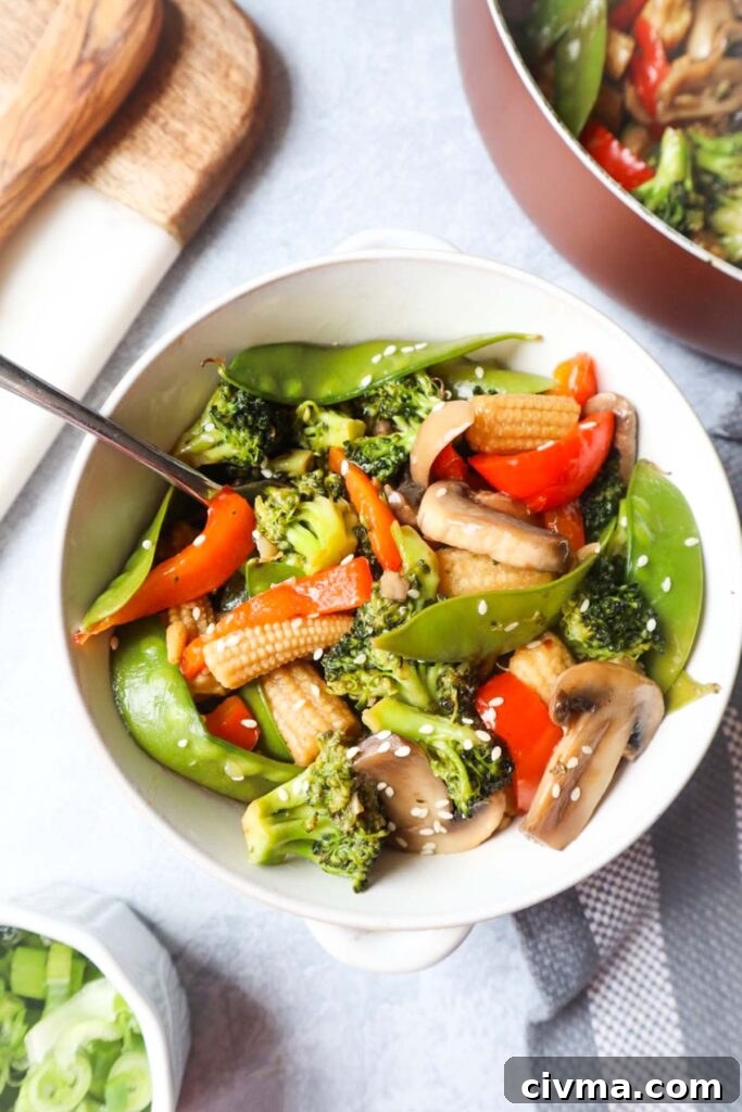 white bowl with pad pad thai which contains broccoli, snow peas, red bell peppers, mushrooms, carrot topped with sesame seeds