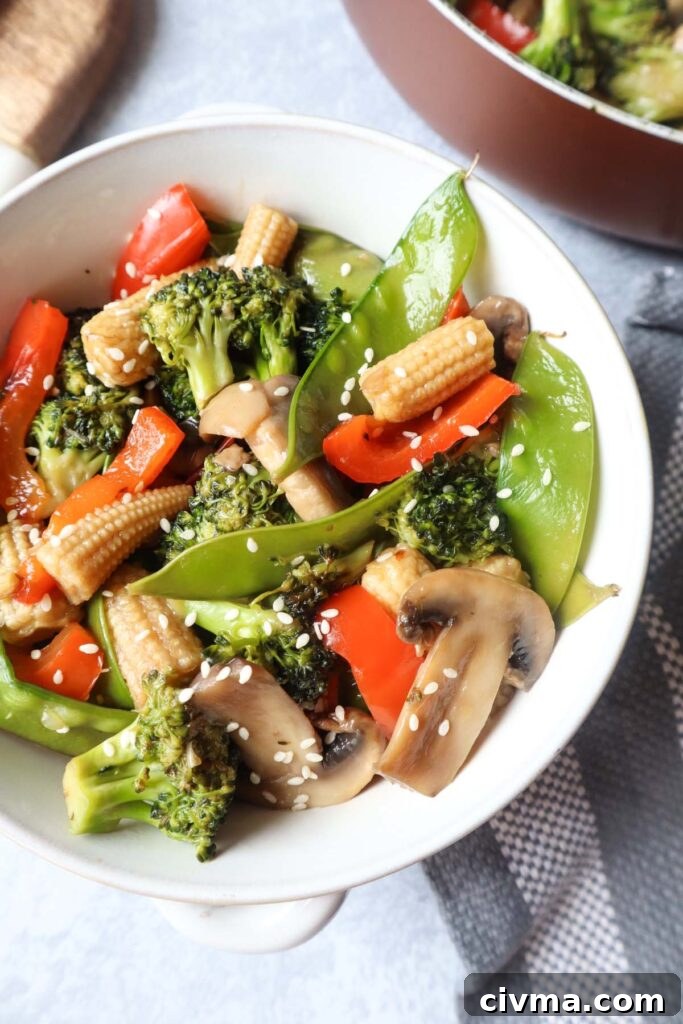 white bowl with pad pad thai which contains broccoli, snow peas, red bell peppers, mushrooms, carrot topped with sesame seeds