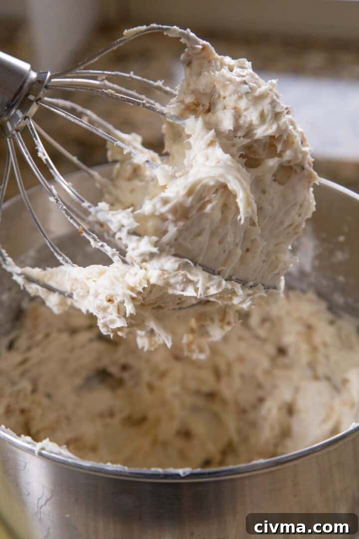 chunky cream cheese frosting with coconut in it, on the beater of a stand mixer.