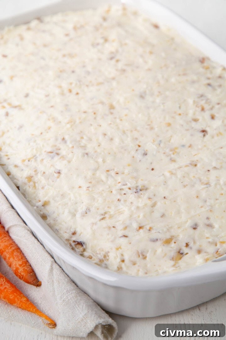 cake frosted with a white coconut cream cheese frosting in a white baking dish.