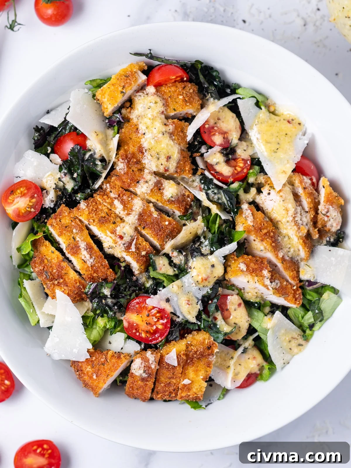 chicken tender salad in a white bowl with green lettuce, kale, tomatoes, fried chicken tenders, shaved parmesan and parmesan vinaigrette