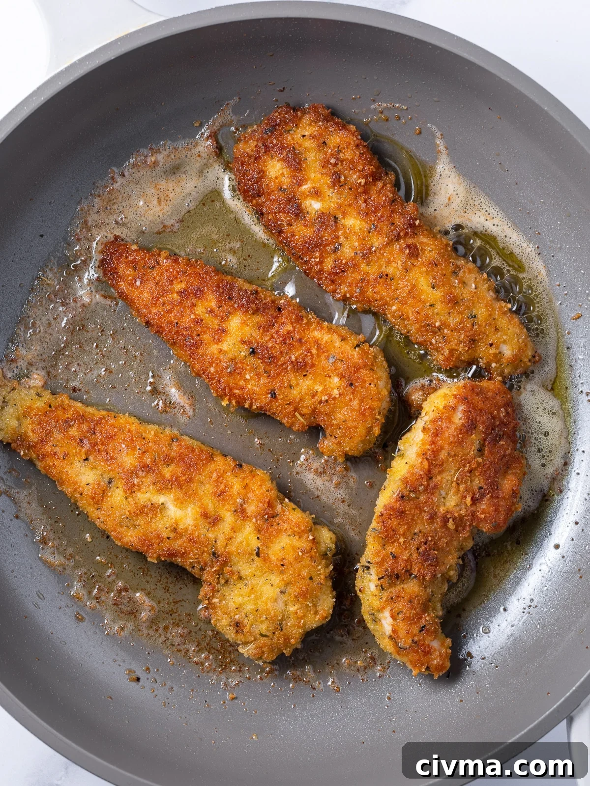 crispy parmesan-crusted chicken tenders cooking in a large skillet in some olive oil