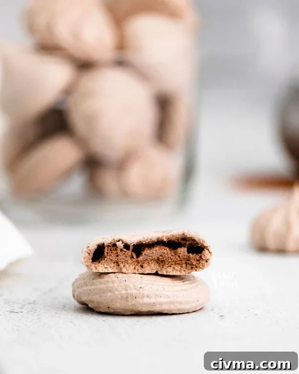 two dark chocolate meringue cookies stacked on top of each other with the top one cut in half to show the interior