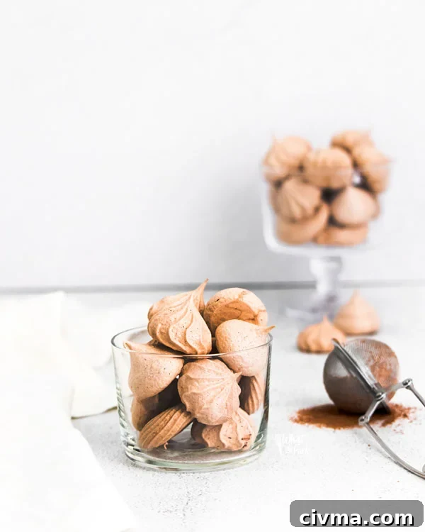 straight on shot of dark chocolate meringue cookies in a clear glass cup with more cookies in the background