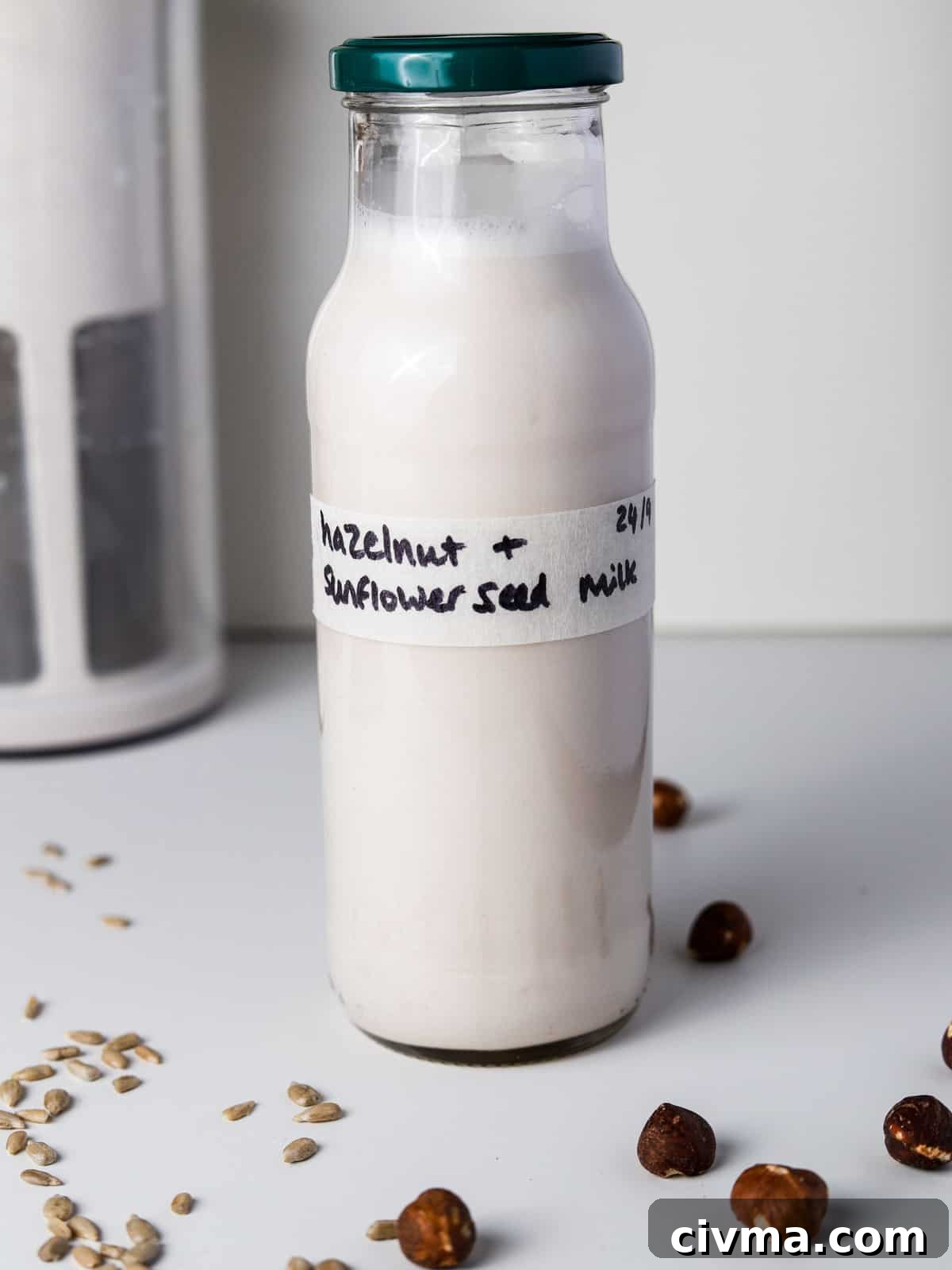 Hazelnut Sunflower Seed Milk Recipe 6 Photo of a bottle of hazelnut and sunflower seed milk with a a few hazelnuts and sunflower seeds strewn around.