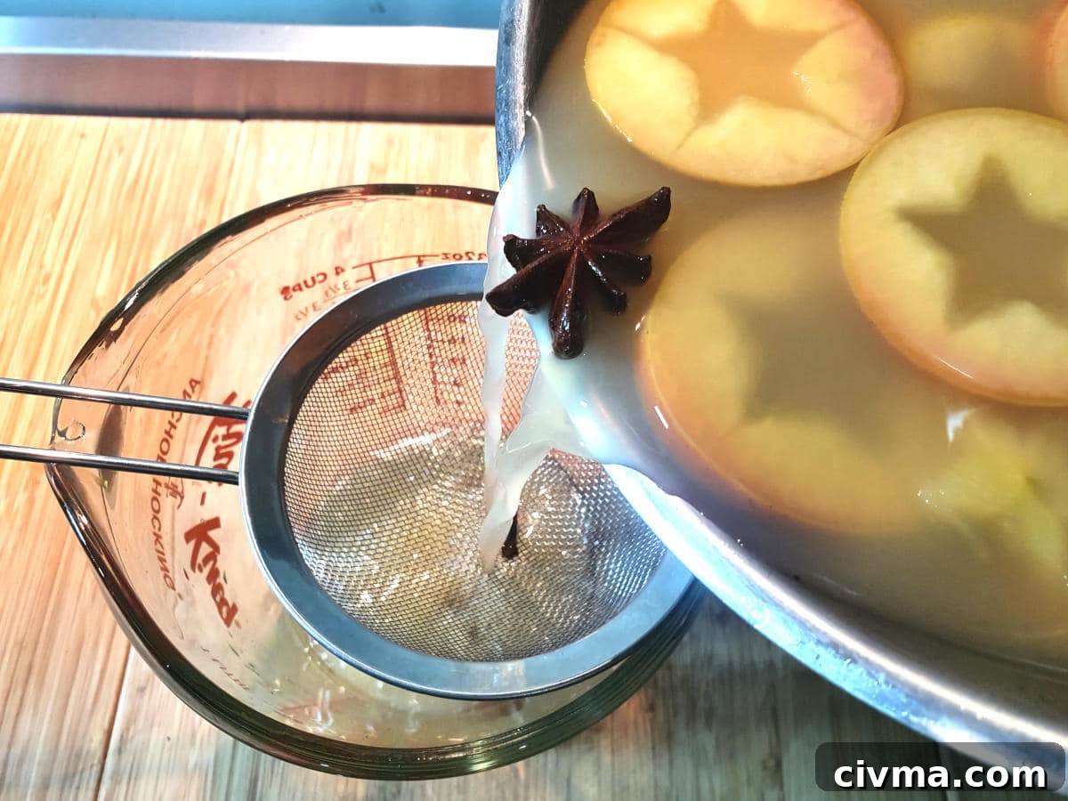 Straining cooled apple cider through a sieve into a heatproof jug.