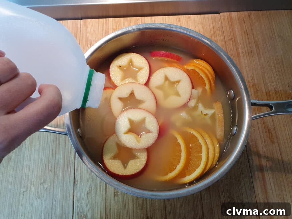 Pouring apple cider into pot with sliced apple and oranges.
