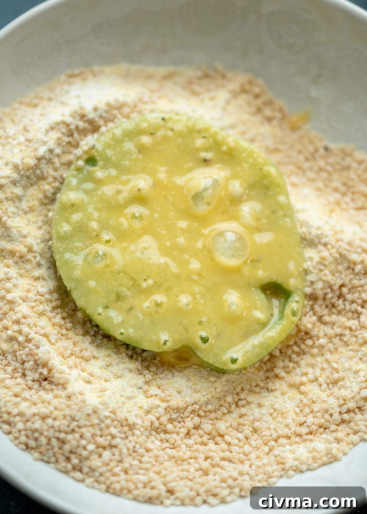 green tomato slice covered in egg wash, laying in a bowl of cornmeal breading