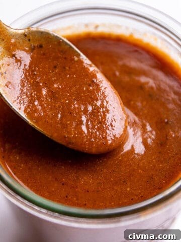 A spoon scooping enchilada sauce out of a glass jar.