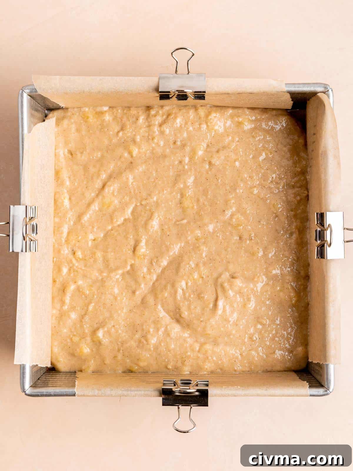 Banana cake batter in an 8x8 inch pan lined with parchment paper.