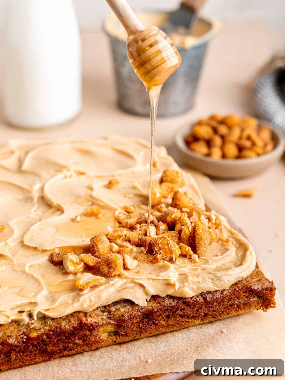 Drizzling honey on top of a banana snack cake with peanut butter honey frosting.